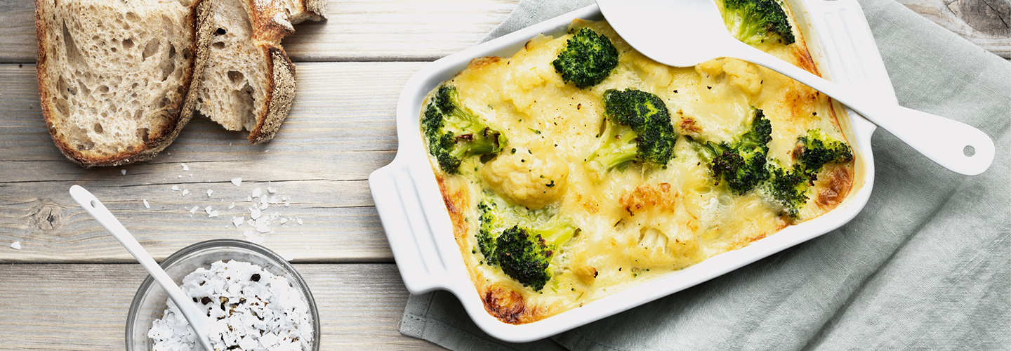 Brokkoli- og grønnsaksgrateng med ost i ildfast form, brødskiver ved siden av.