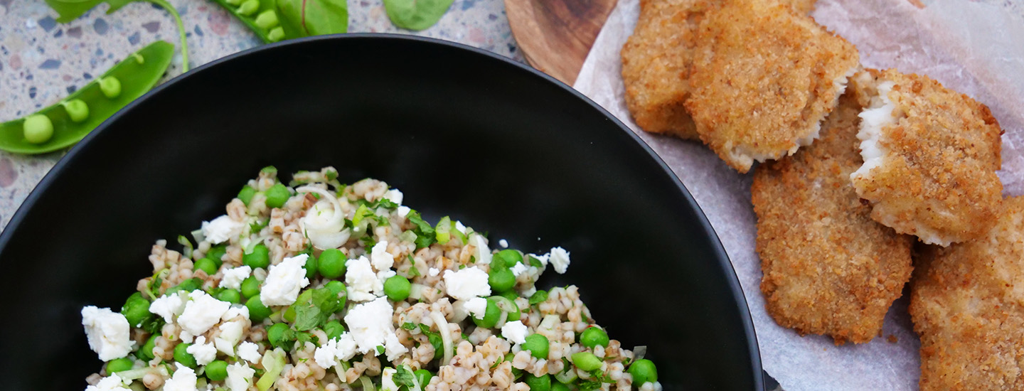 Sort bolle med byggrynssalat med erter og feta, servert som tilbehør til sprø fiskefileter